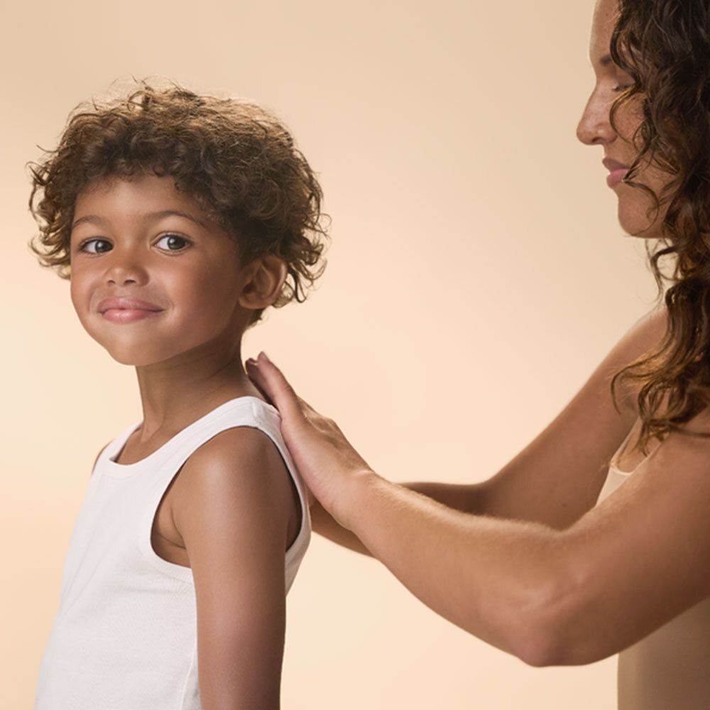 Enfant avec crème solaire sur le dos. Main sur l'épaule de l'enfant.