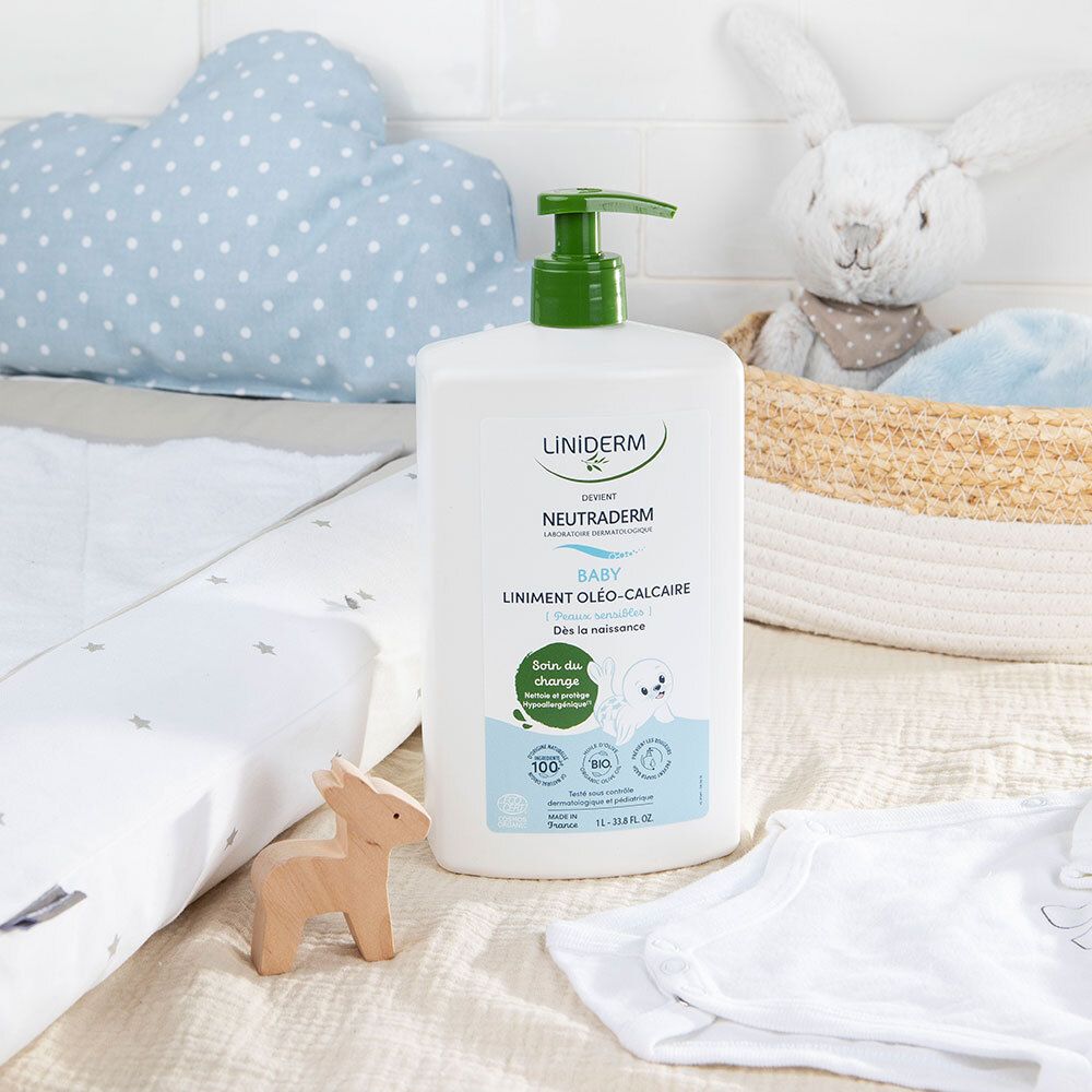 Flacon blanc avec pompe verte sur un matelas à langer. Articles pour bébé en arrière-plan. Produit : LINIDERM NEUTRADERM BABY.