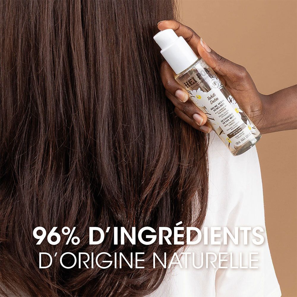 Main appliquant la Brume Démêlante HEI POA Tahiti Detox sur de longs cheveux foncés.
