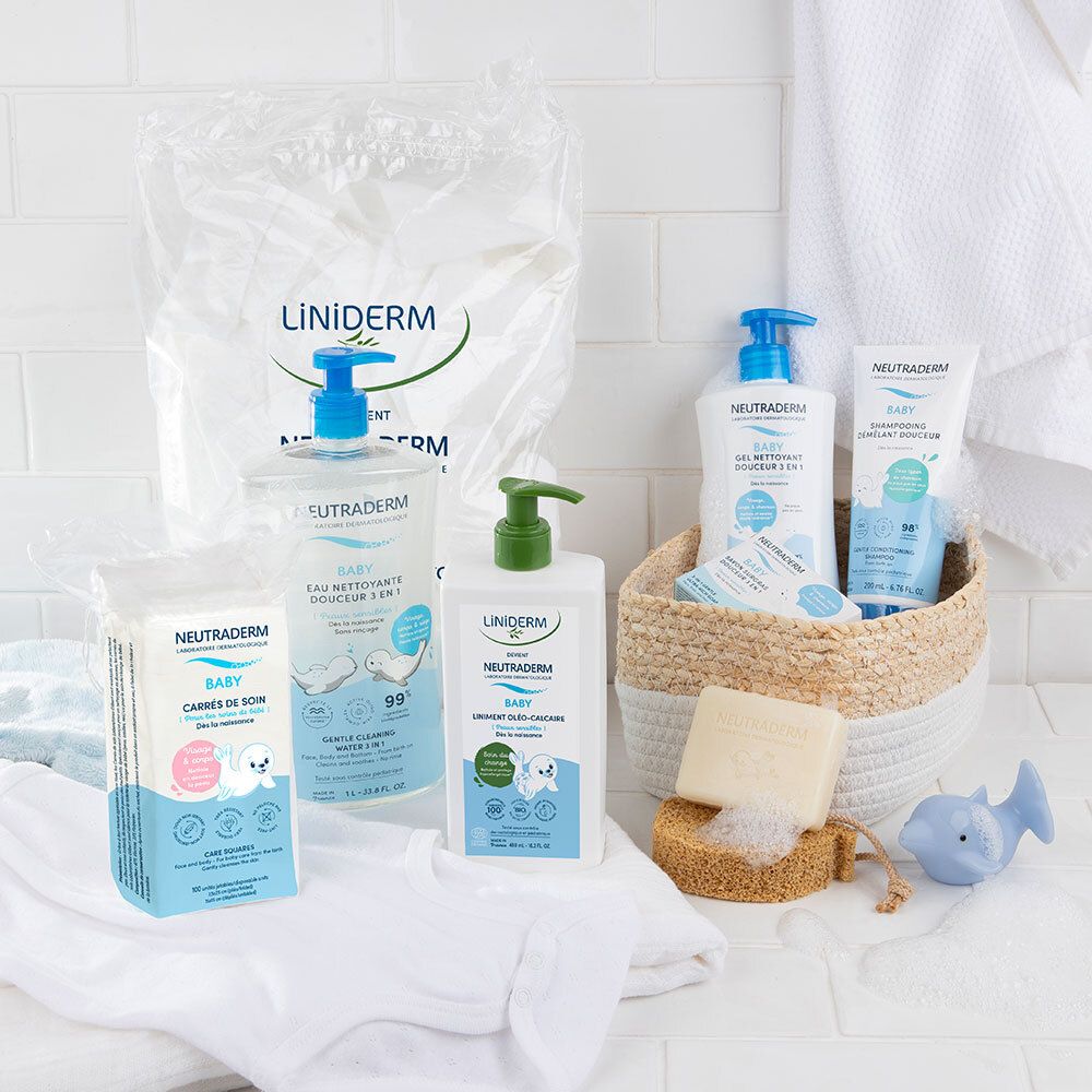 Plusieurs produits LINIDERM sur une surface blanche. Bouteilles, pads, savon et un panier. Gamme bébé.