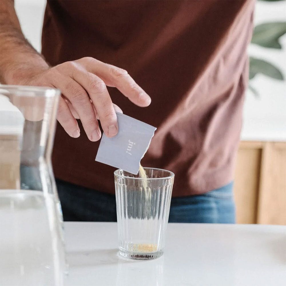 Person gießt Pulver aus einem Beutel in ein Glas. Der Beutel trägt die Aufschrift "jm!".