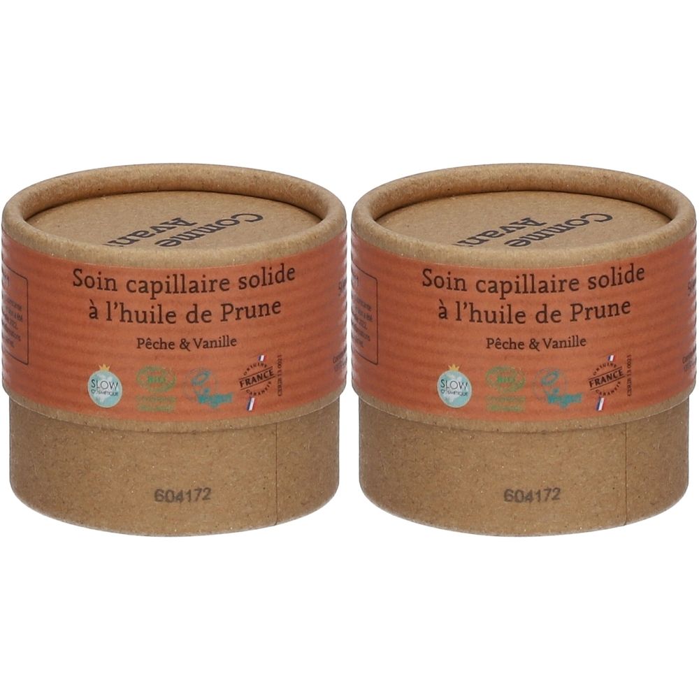 Zwei zylindrische Behälter aus braunem Karton. Aufschrift: Soin capillaire solide à l'huile de Prune, Pêche & Vanille. Mit Zertifizierungen.