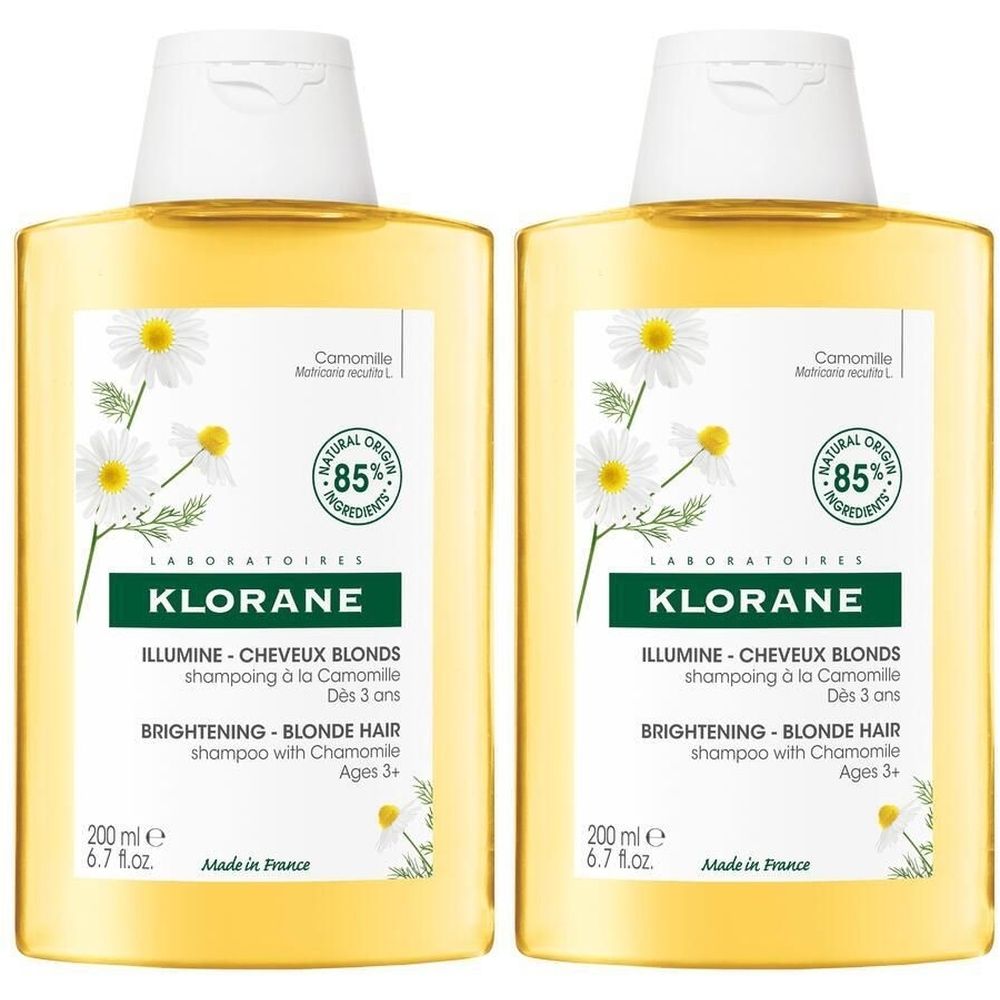 Deux flacons de shampoing jaunes avec bouchon blanc. Étiquettes avec fleurs de camomille, texte: KLORANE, ILLUMINE-CHEVEUX BLONDS, 85% ingrédients naturels.