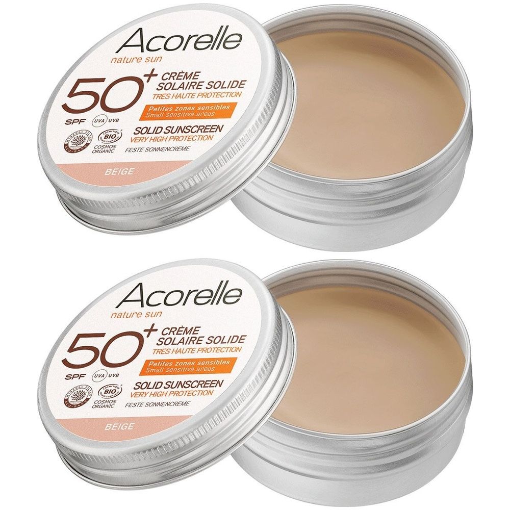 Deux boîtes rondes argentées avec crème beige. Couvercles avec texte: Acorelle, SPF 50+, Crème Solaire Solide, Beige.