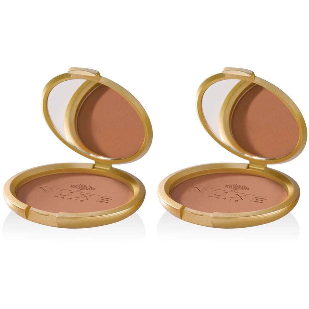 Zwei goldfarbene Puderdosen mit Spiegel und braunem Puder. Auf dem Puder ist der Markenname Nuxe zu sehen.