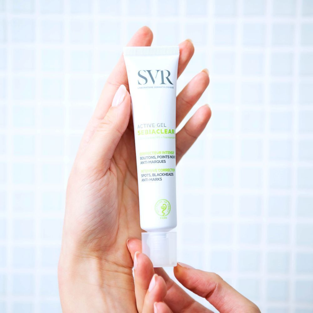 Une main tient un tube de SVR SEBIACLEAR Active Gel. Tube blanc avec texte vert et noir. Logo SVR.