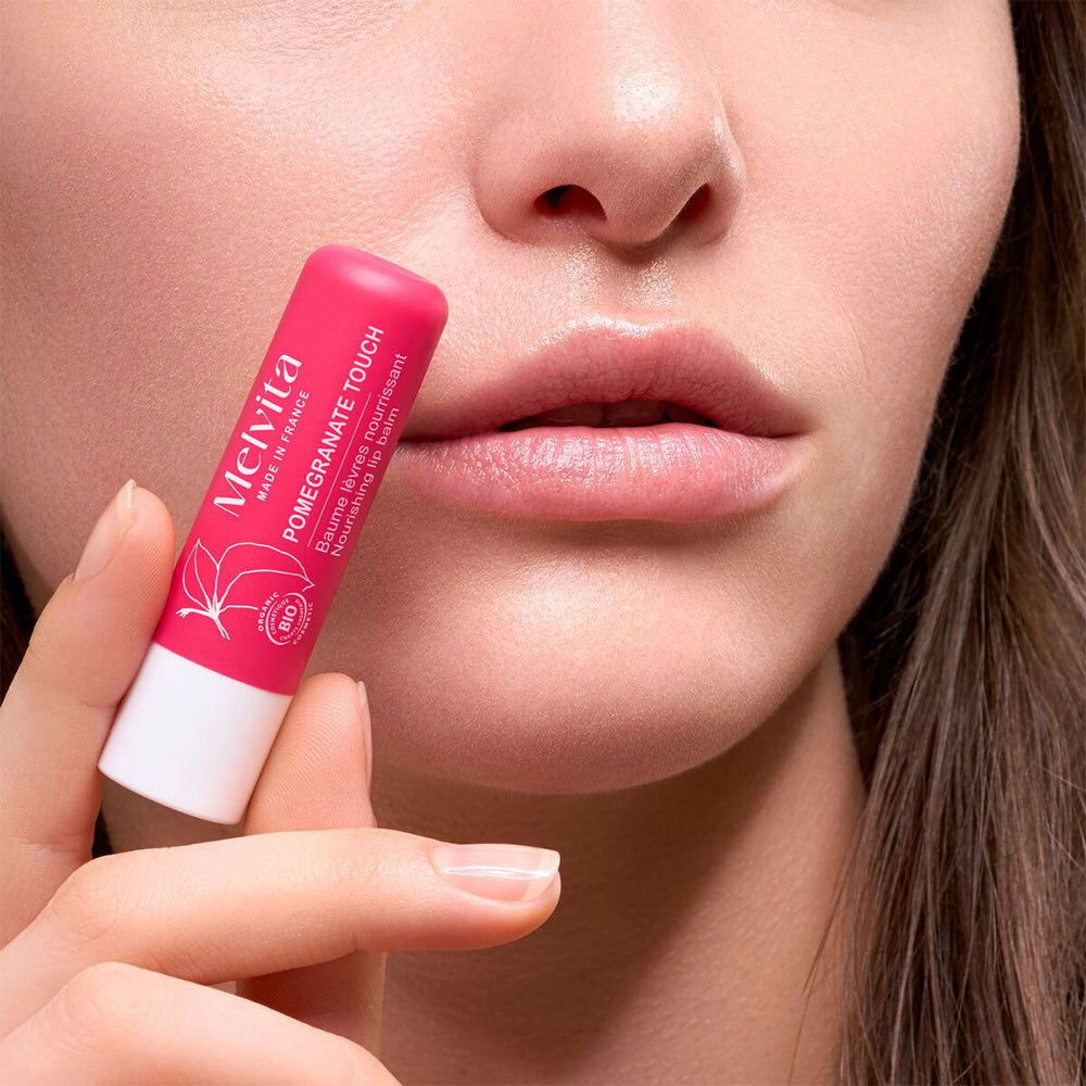 Person hält rosa Lippenbalsam-Stift vor Lippen. Auf dem Stift steht: Pomegranate Touch, Melvita, Bio-Siegel.