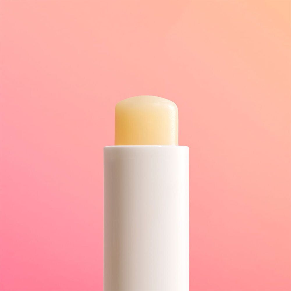 Nahaufnahme eines weißen Lippenbalsam-Stifts mit gelbem Balsam. Der Stift ist auf rosa Hintergrund platziert.