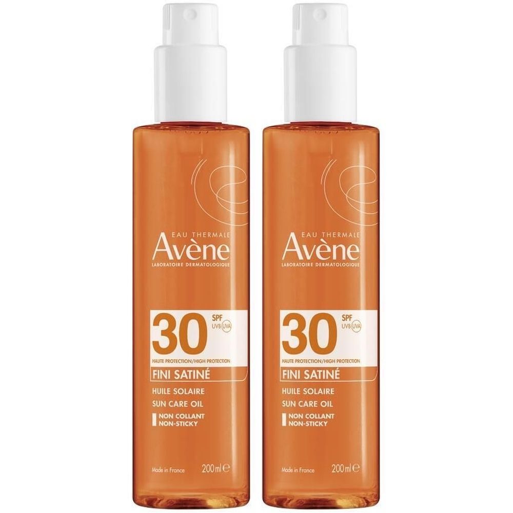 Deux flacons d'huile solaire avec vaporisateur blanc. Inscriptions: Avène, SPF 30, Huile Solaire, Fini Satiné. Liquide orangé visible.