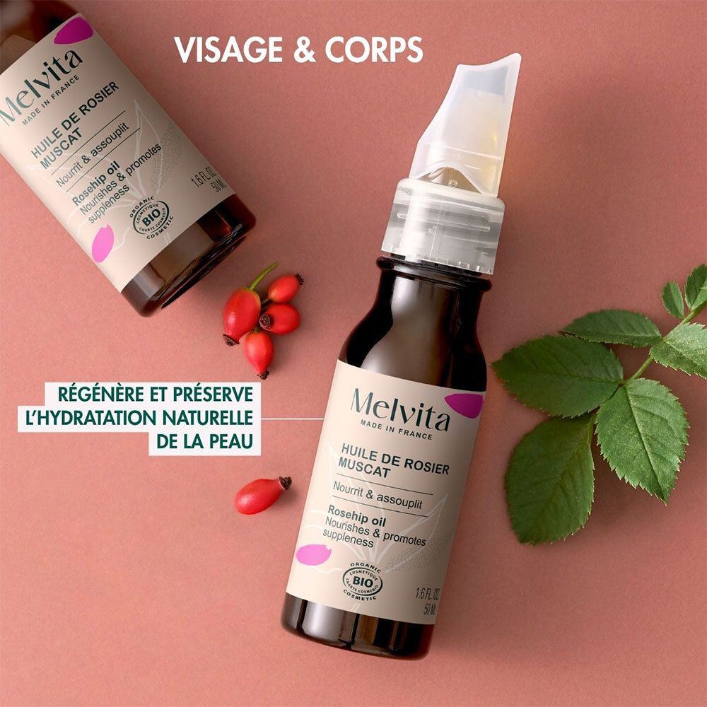 Deux flacons Melvita Huile de Rosier Muscat. À côté, des cynorhodons et des feuilles. Texte: Visage & Corps, certification Bio.