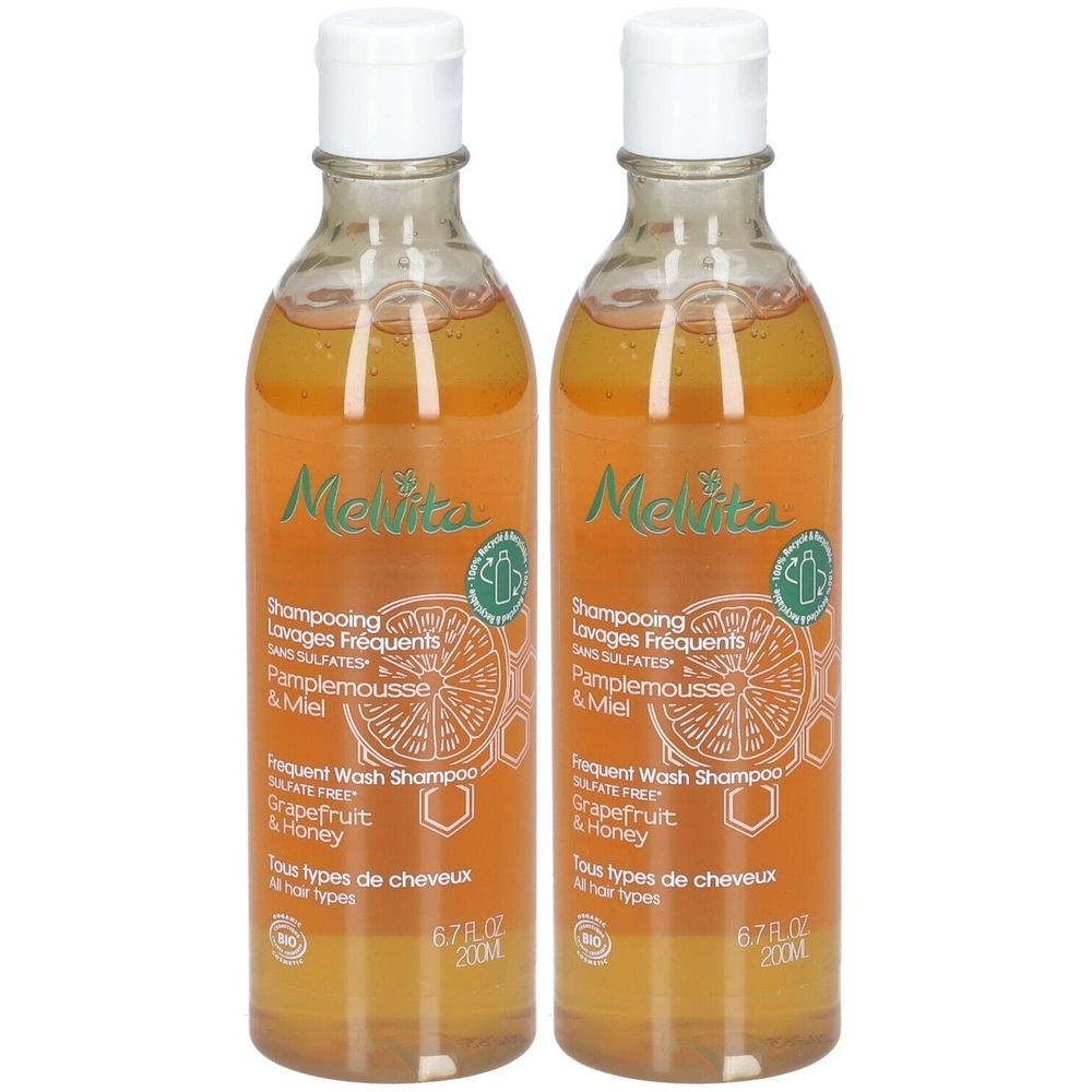 Deux flacons de shampooing Melvita. Flacons transparents avec bouchons blancs. Étiquettes avec informations produit et logo. Pamplemousse et miel.