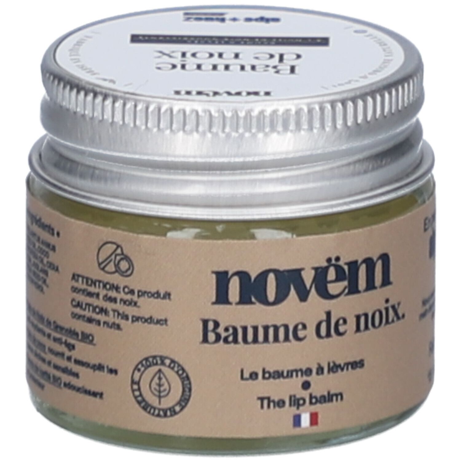 Glas mit silbernem Deckel. Aufkleber mit Produktnamen: novëm Baume de noix. Le Baume à lèvres. The lip balm. Enthält Nüsse. Flagge Frankreich.