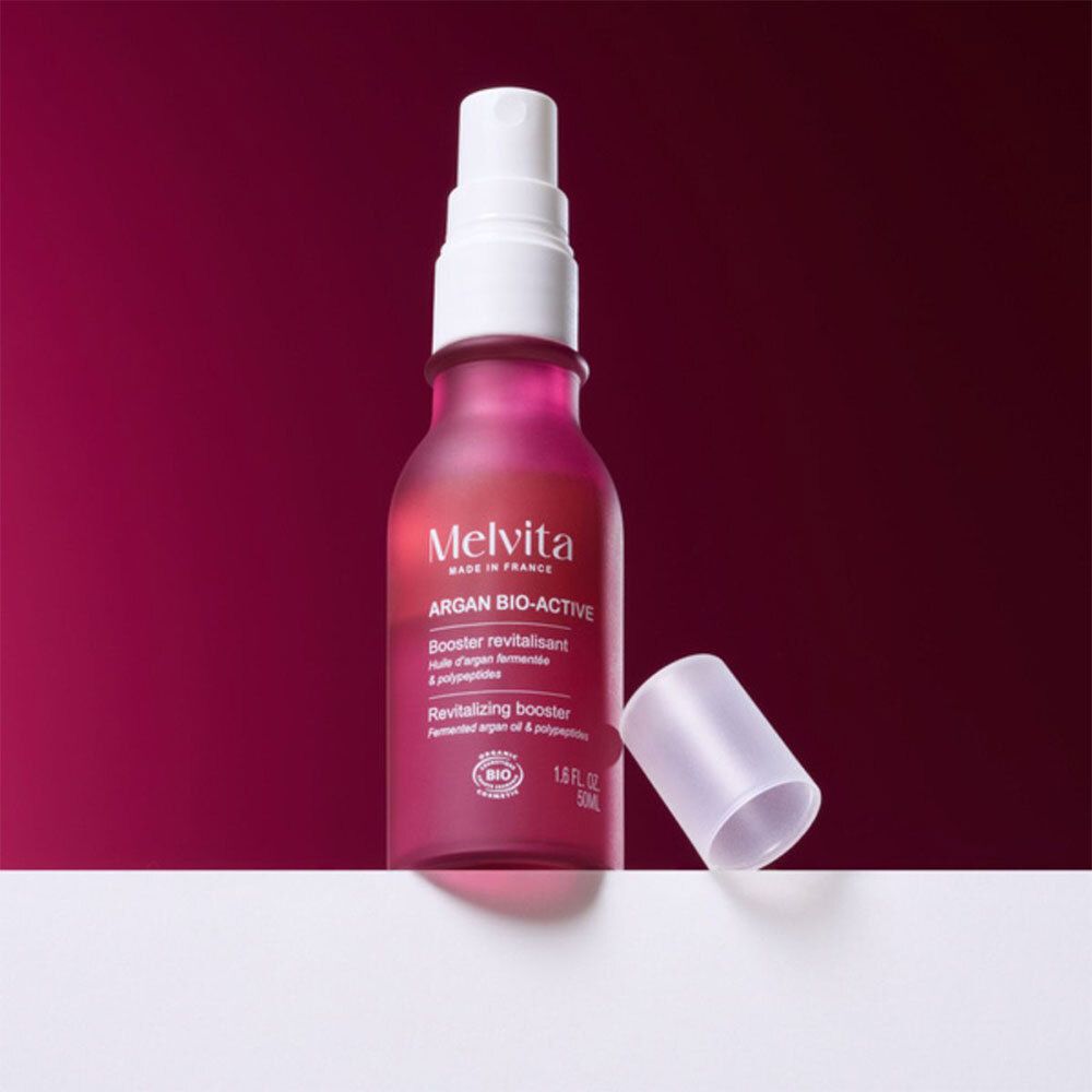 Flacon rouge avec vaporisateur et bouchon séparé. Inscription: Melvita Argan Bio-Active.