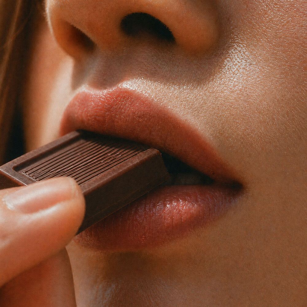 Nahaufnahme von Lippen, die ein Stück dunkle Schokolade essen.