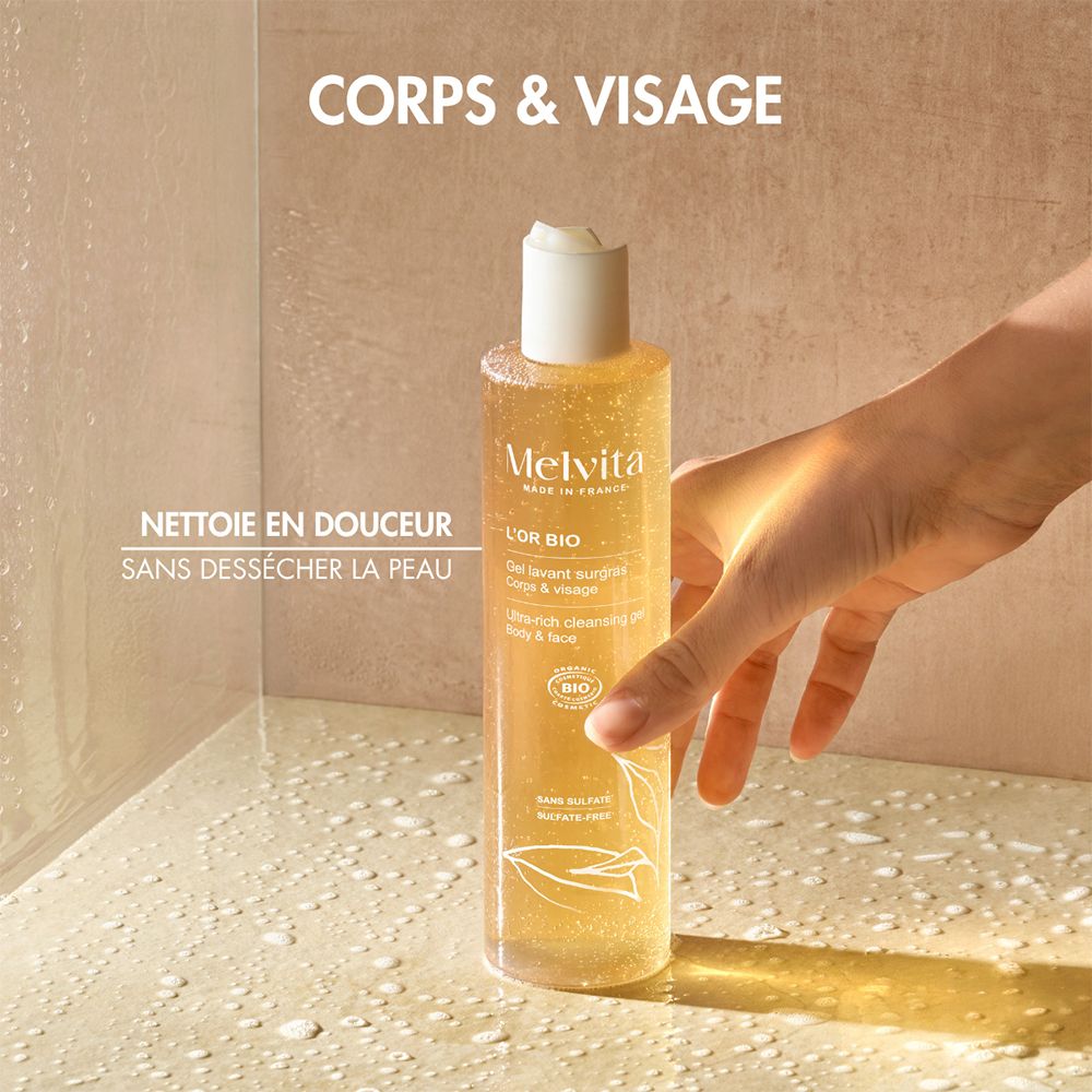 Melvita Duschgel in Flasche, gehalten von einer Hand in einer Dusche. Text: "CORPS & VISAGE".