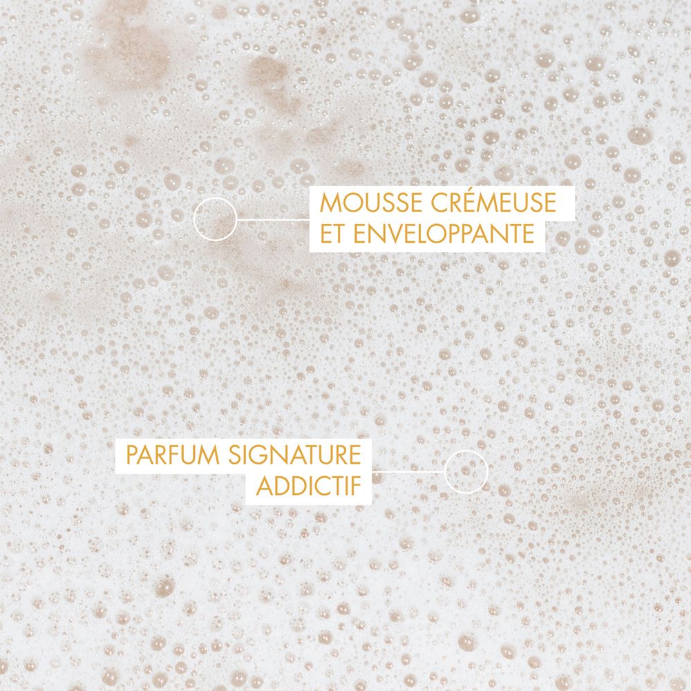 Nahaufnahme von reichhaltigem Schaum mit Blasen. Text: "MOUSSE CRÉMEUSE ET ENVELOPPANTE" und "PARFUM SIGNATURE ADDICTIF".