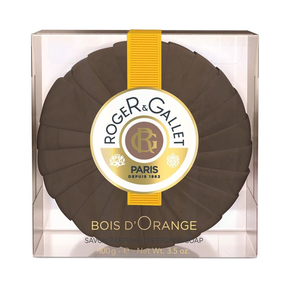 Savon rond dans boîte transparente. Logo et nom du produit visibles. Savon avec surface cannelée. "Bois d'Orange" clairement visible.