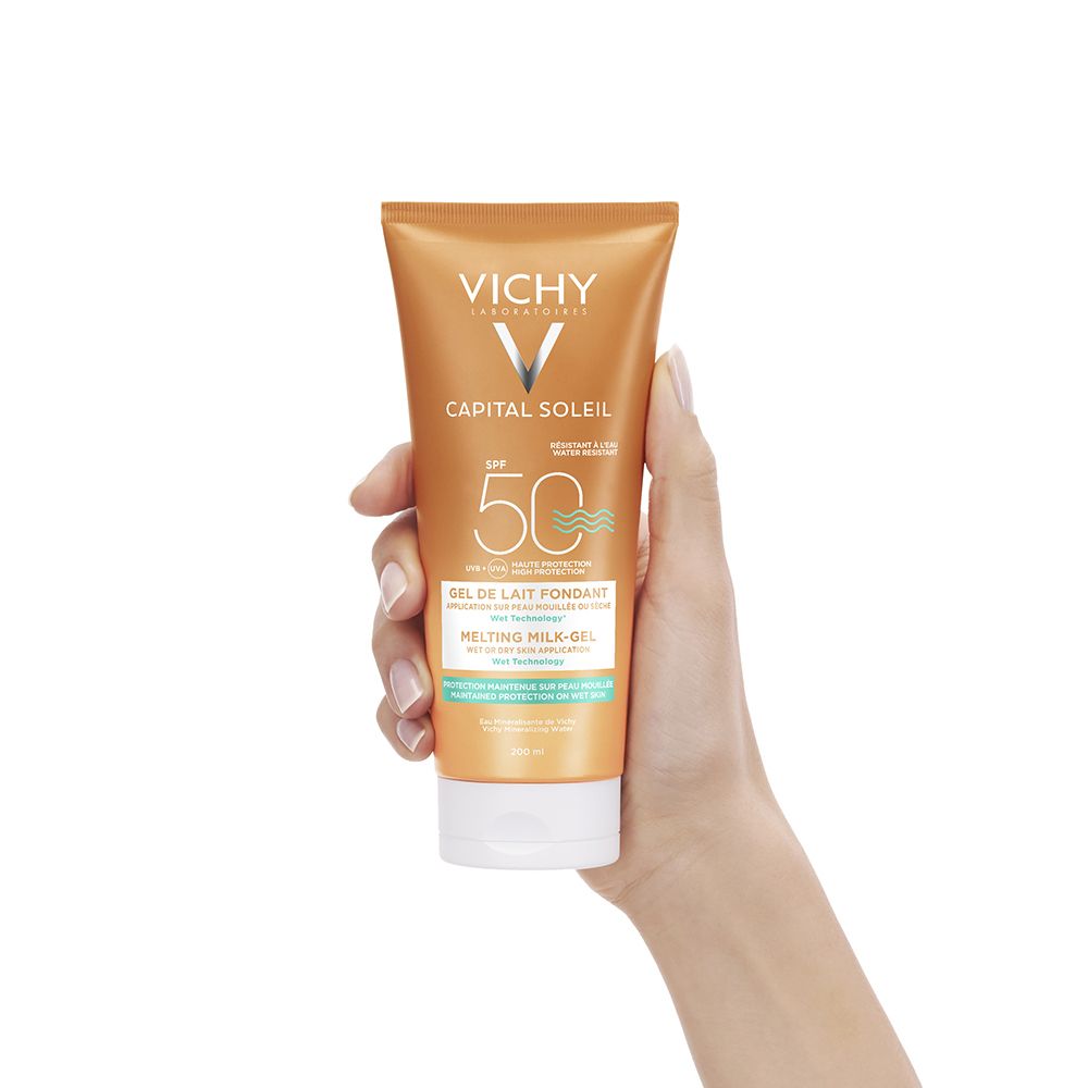 Goldfarbene Sonnenmilch-Gel-Tube mit weißem Verschluss, gehalten von einer Hand. Aufschrift: VICHY, CAPITAL SOLEIL, SPF 50.
