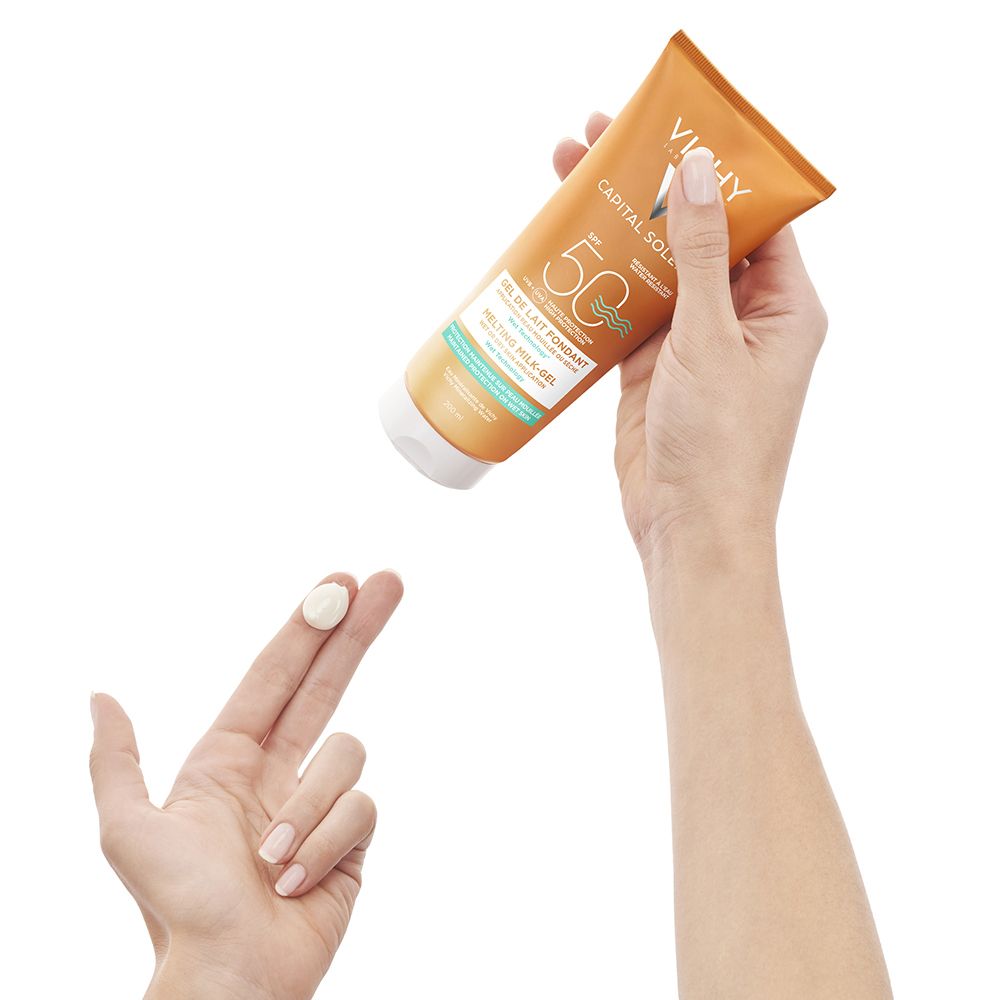 Goldfarbene Sonnenmilch-Gel-Tube mit weißem Verschluss, gehalten von einer Hand. Auf einem Finger befindet sich eine Spur des Produkts.