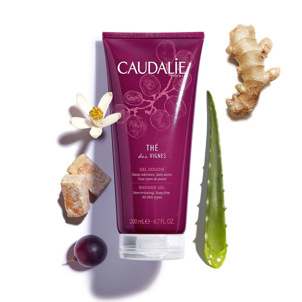 Tube de gel douche rouge foncé, avec gingembre, aloe vera, raisin, fleur et cubes. Inscription CAUDALIE, Thé des Vignes.
