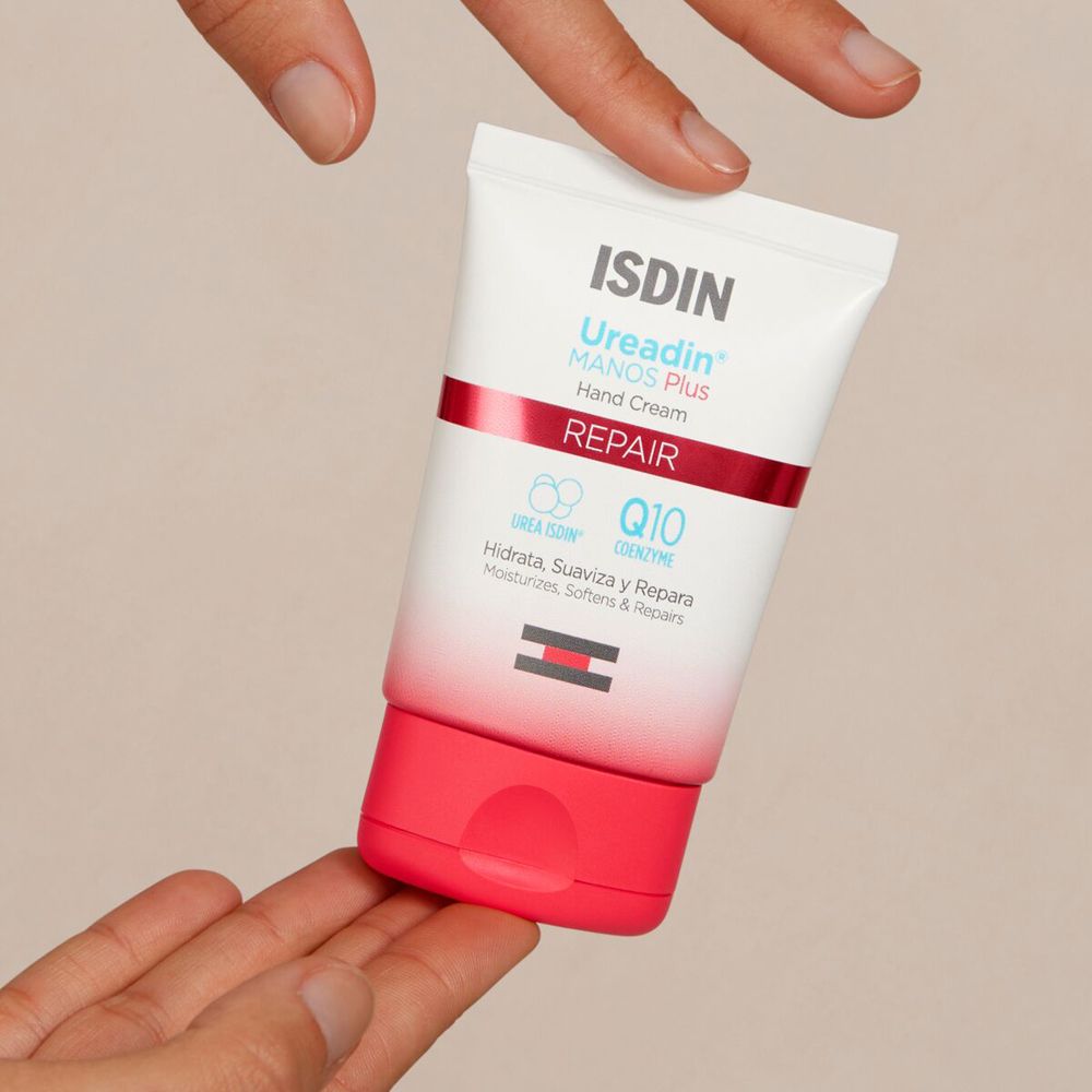Mains tenant un tube de crème pour les mains. Inscription: ISDIN Ureadin® MANOS PLUS Hand Cream REPAIR.