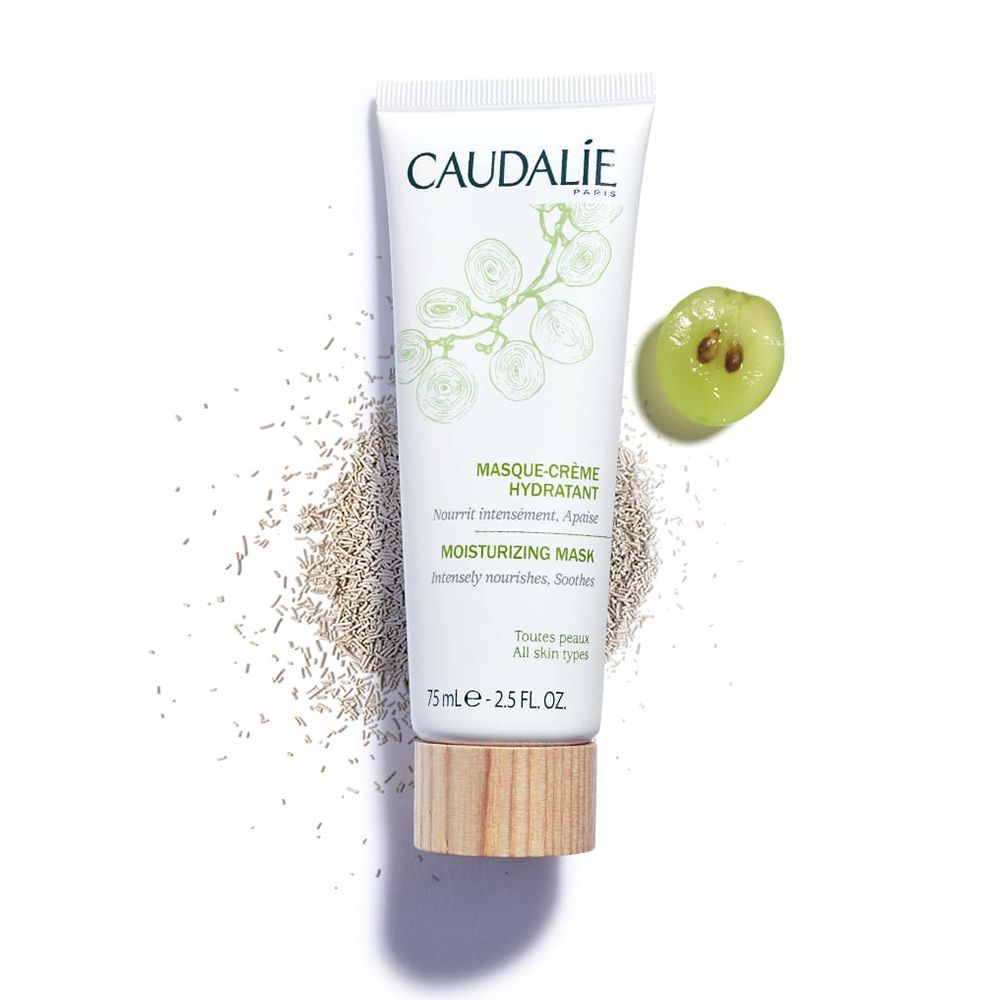 Weiße Tube mit grünem Aufdruck. Text: CAUDALIE, MASQUE-CRÈME HYDRATANT, MOISTURIZING MASK. Holzfarbener Boden. Traube und Samen.