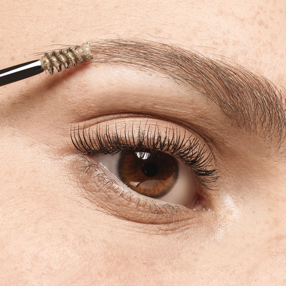 Œil avec sourcils travaillés avec une brosse. La brosse est recouverte d'un produit.