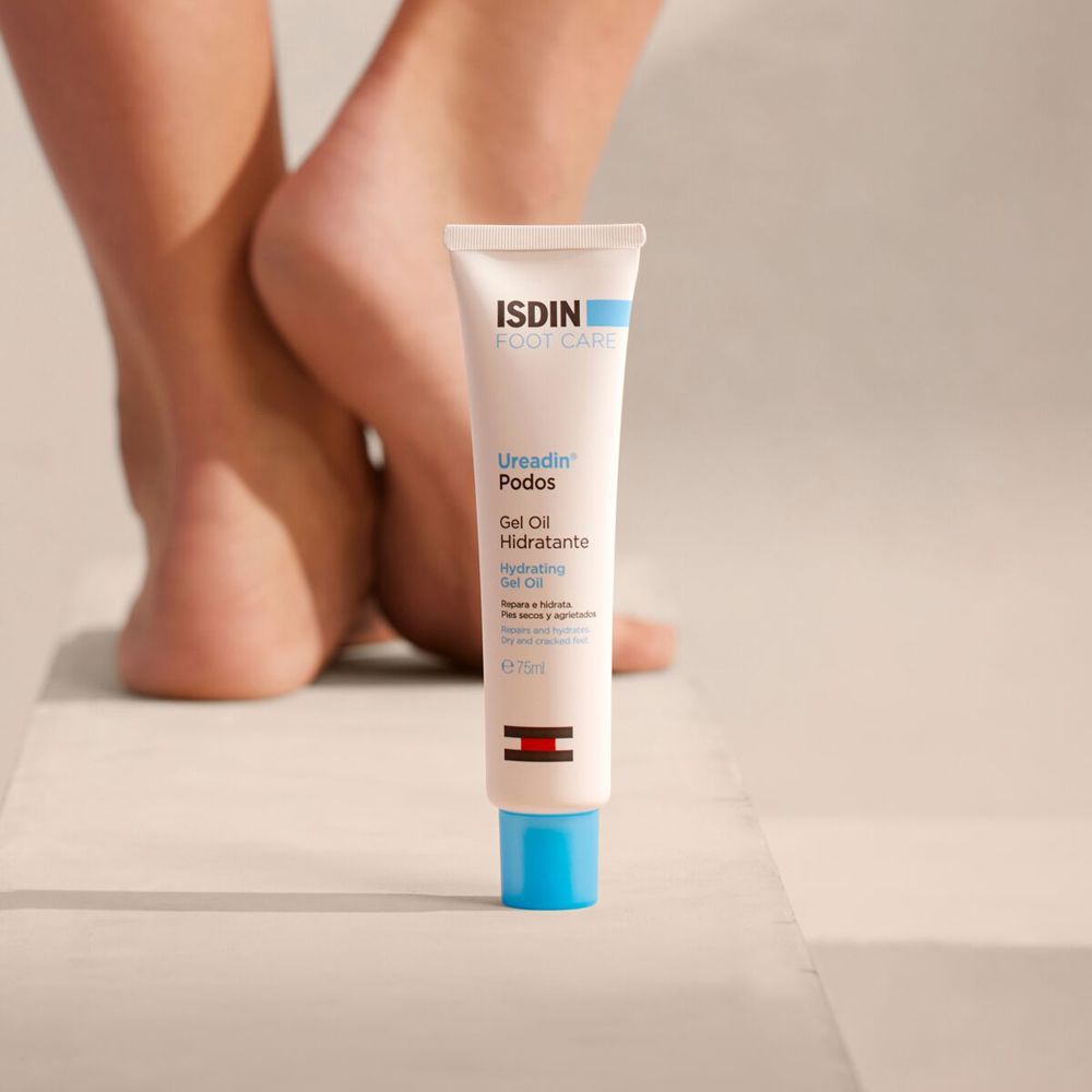Tube von ISDIN Foot Care Ureadin Podos Gel Oil neben Füßen. Der Hintergrund ist unscharf.