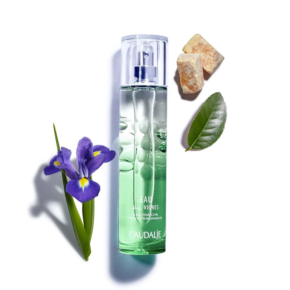 Flacon de parfum vert, à côté: fleur d'iris, feuilles, morceaux de sucre. Inscription: Eau des Vignes, Caudalie.