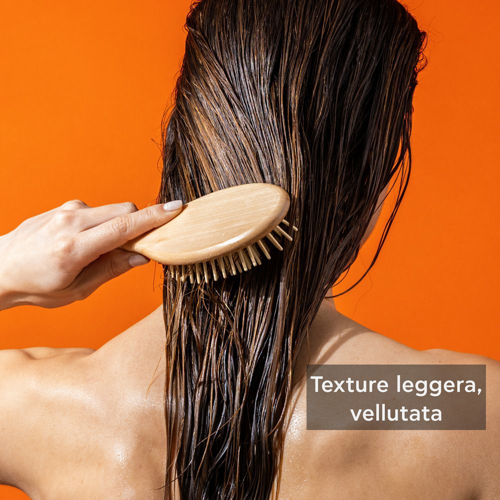 Personne brosse les cheveux mouillés avec une brosse en bois. Texte: Texture leggera, vellutata.