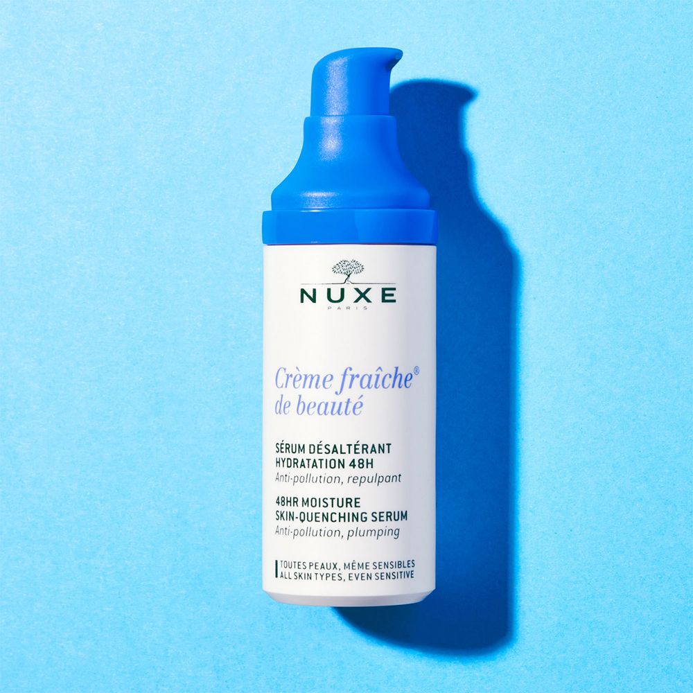 Serumflasche mit blauem Pumpkopf. Aufschrift: Nuxe Crème fraîche de beauté. Hintergrund: hellblau.