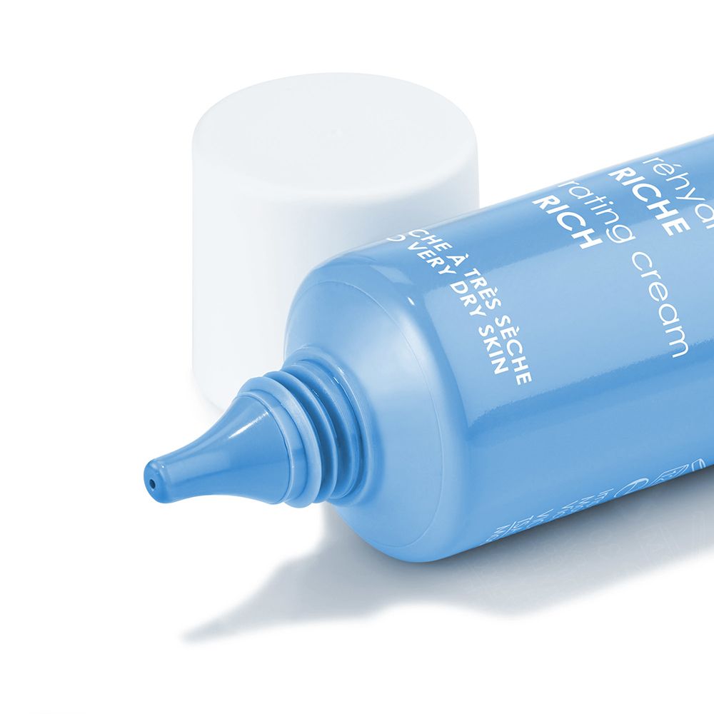 Gros plan d'un tube bleu avec bouchon blanc. Texte : Crème réhydratante Riche. Embout du tube visible.