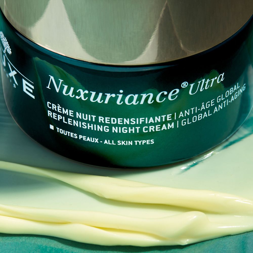 Gros plan du produit. Inscription: Nuxuriance Ultra, crème de nuit. Texture crème sur surface claire.