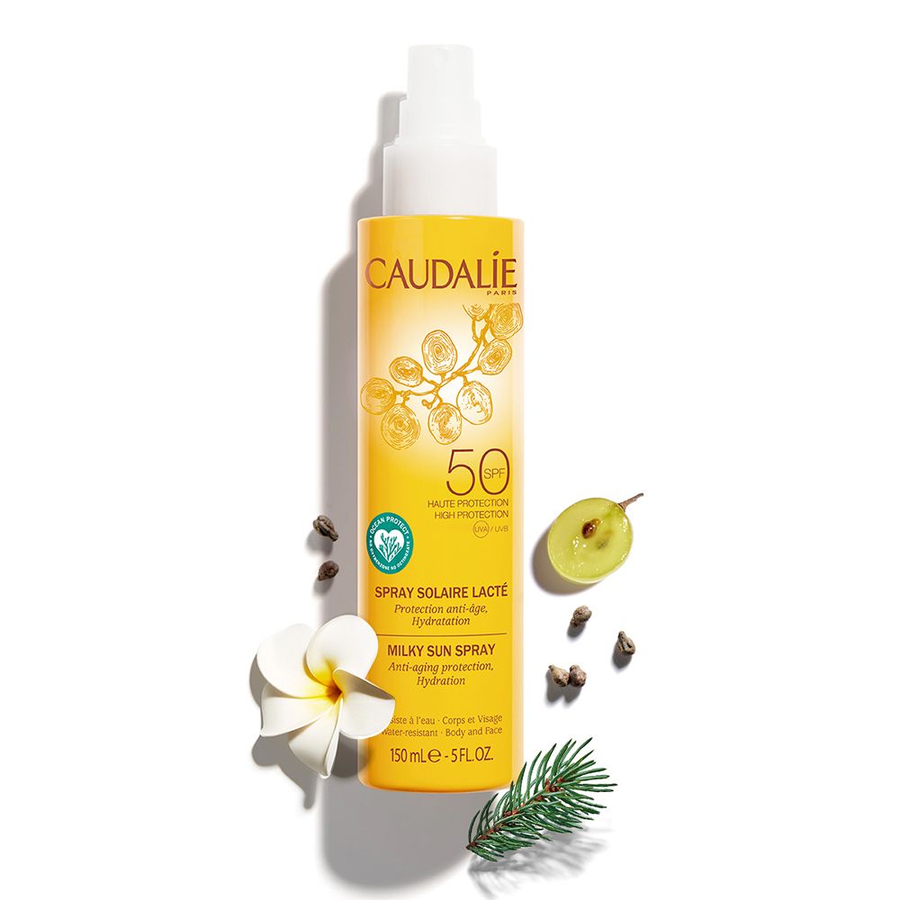 Flacon spray solaire jaune avec éléments blancs. Inscriptions: CAUDALIE, SPF50, Spray Solaire Lacté. Avec fruits.