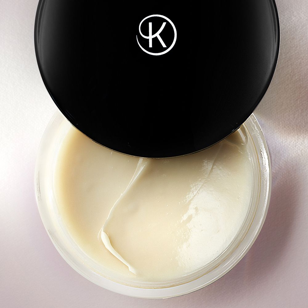 Geöffneter Creme-Tiegel. Cremige, helle Creme sichtbar. Schwarzer Deckel mit Logo.