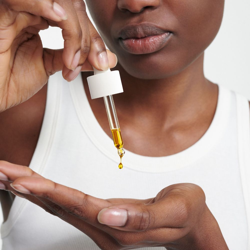 Person hält Pipette mit Öl über Handfläche. Öl tropft aus Pipette.