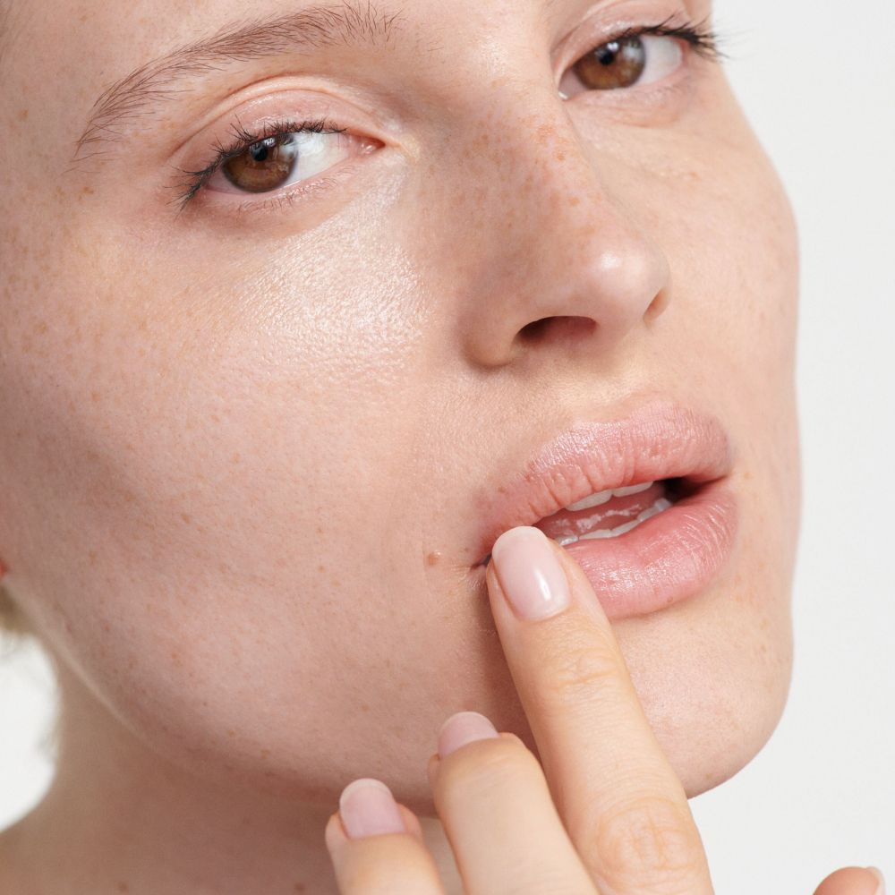 Nahaufnahme von Lippen, auf die Creme aufgetragen wird. Finger berührt die Lippe.