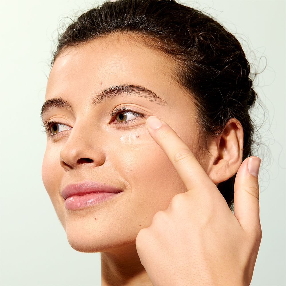 Nahaufnahme einer Frau, die mit dem Finger Creme unter dem Auge aufträgt. Keine Produktbezeichnung sichtbar.