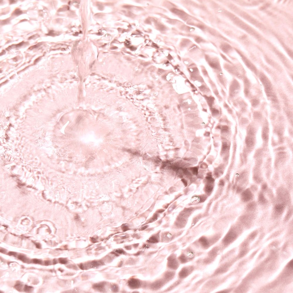 Gros plan d'eau rose avec des ondulations concentriques causées par une goutte.