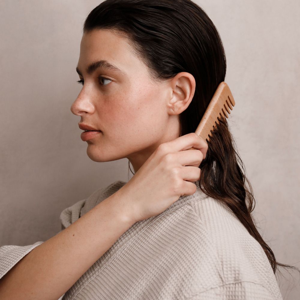 Femme se coiffant les cheveux mouillés avec un peigne en bois. Vue de côté.