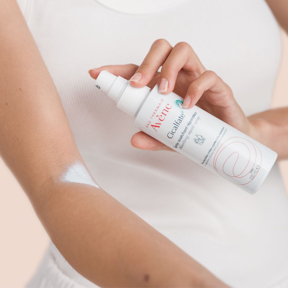 Personne tient spray blanc Eau Thermale Avène. Cicalfate+. Vaporise sur le bras. Pour peaux sensibles.