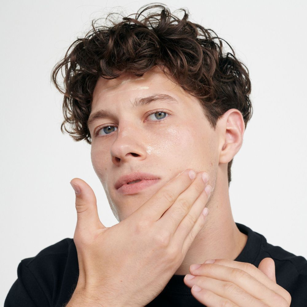 Homme appliquant de la crème sur son visage. Peau claire, cheveux foncés.