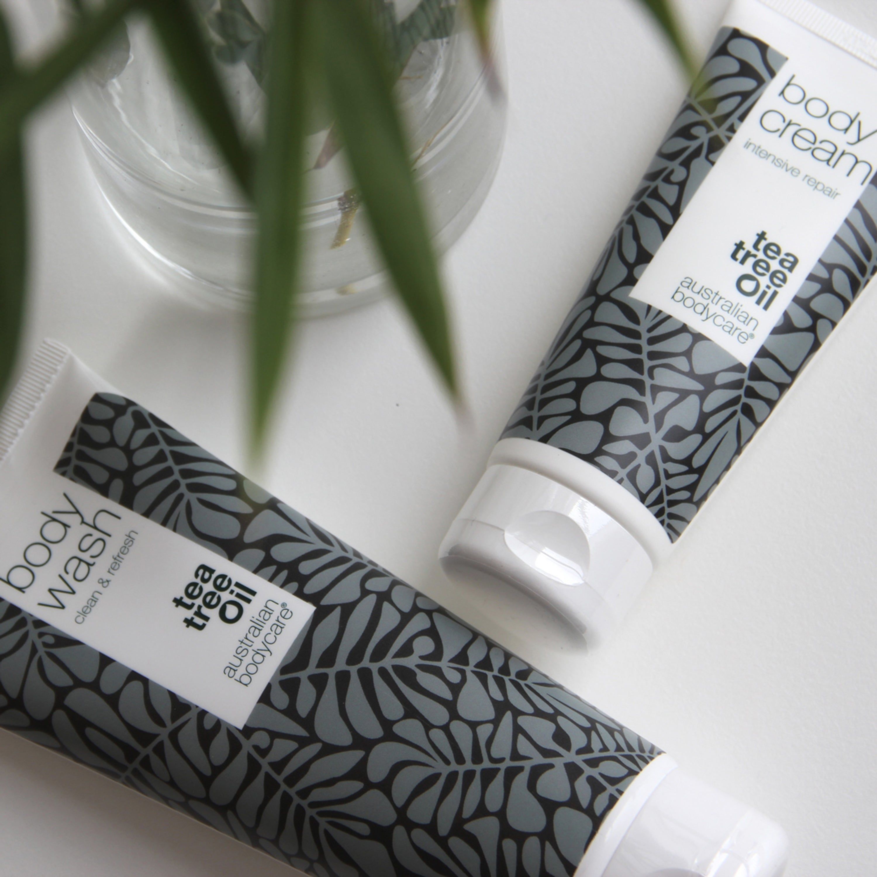 Deux tubes. Inscription : Body Wash, Tea Tree Oil, australian bodycare. Motif feuilles. Sur fond clair.