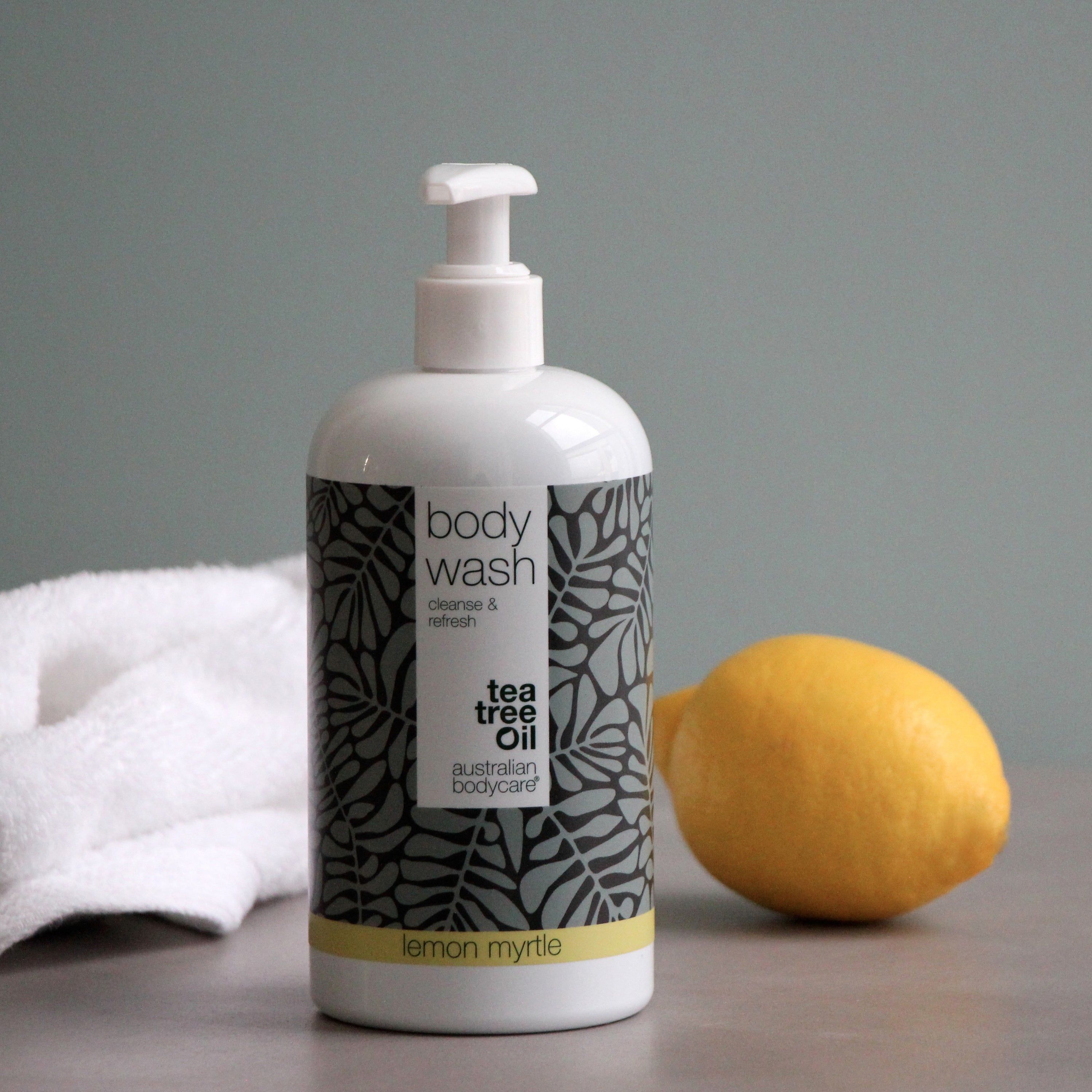 Flacon blanc avec « body wash » et « tea tree oil ». Citron à côté.