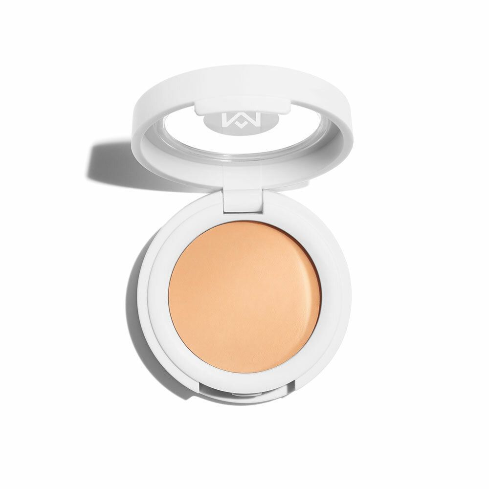 Boîtier de correcteur blanc rond ouvert. Crème beige clair à l'intérieur. Marque avec « M » sur le couvercle.