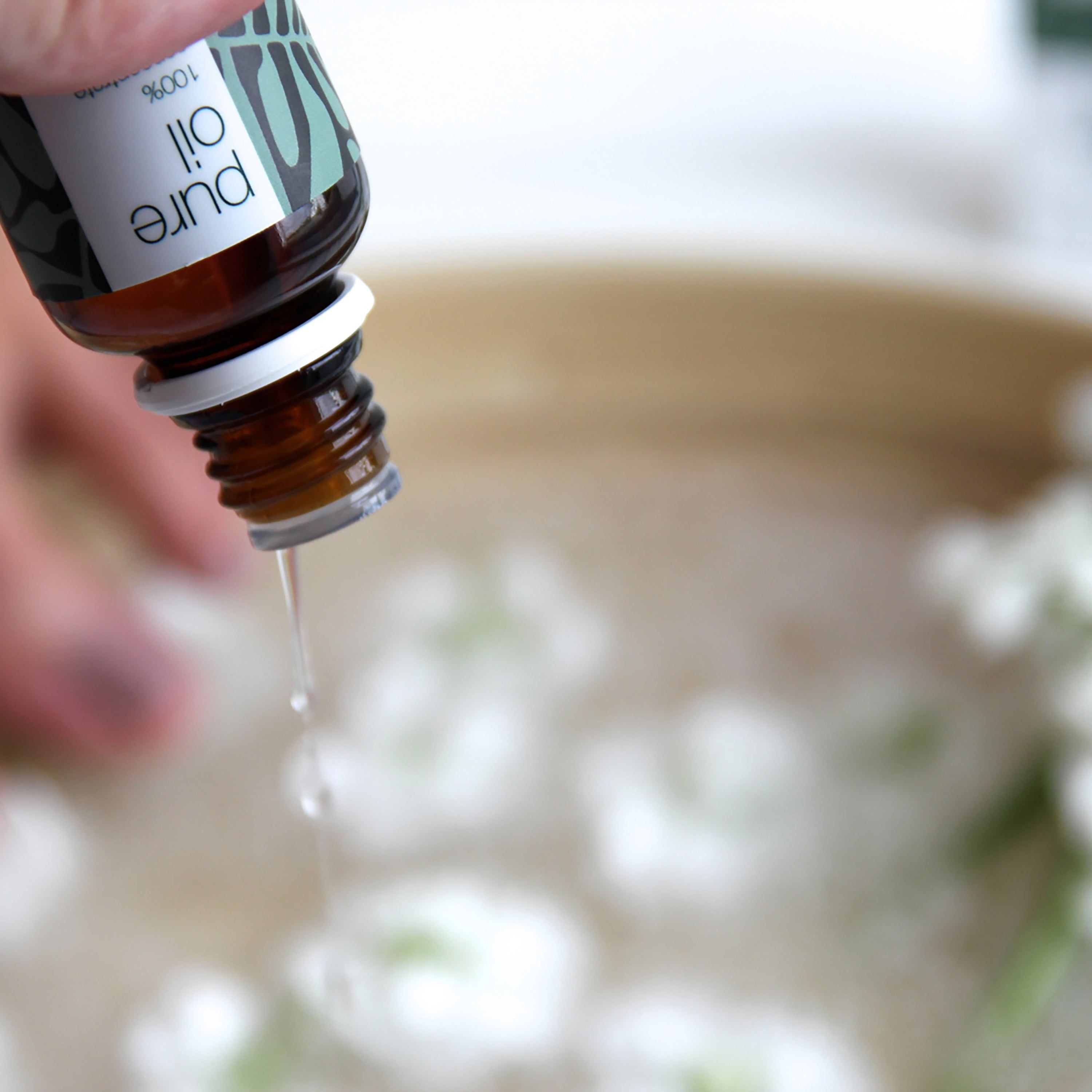 Du liquide d'un flacon en verre brun à bouchon blanc goutte dans un bol. Étiquette : Pure Oil, 100% concentrate.