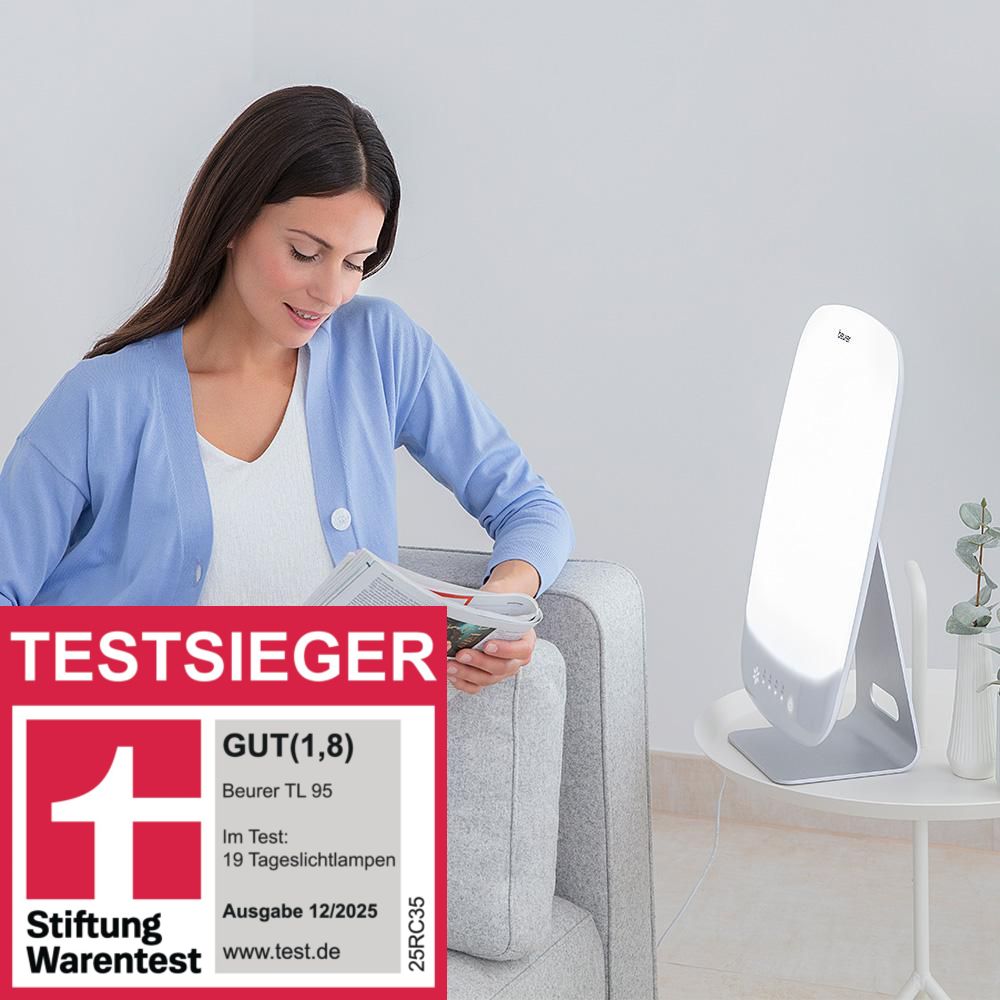 Frau sitzt neben Tageslichtlampe. Auf dem Tisch liegt eine Zeitschrift. Aufkleber: Stiftung Warentest, Note 1,8.