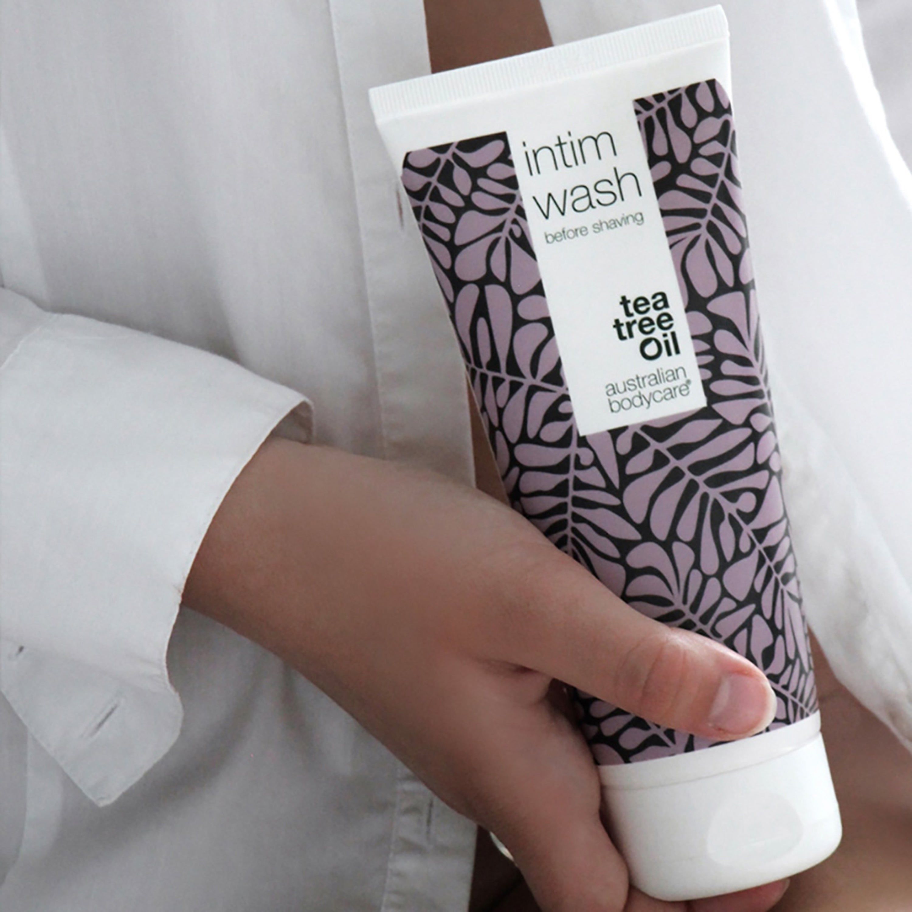 Tube de nettoyant intime. Bouchon blanc, motif de feuilles violet. Inscription : Intim Wash, daily care & before shaving. Dans la main.