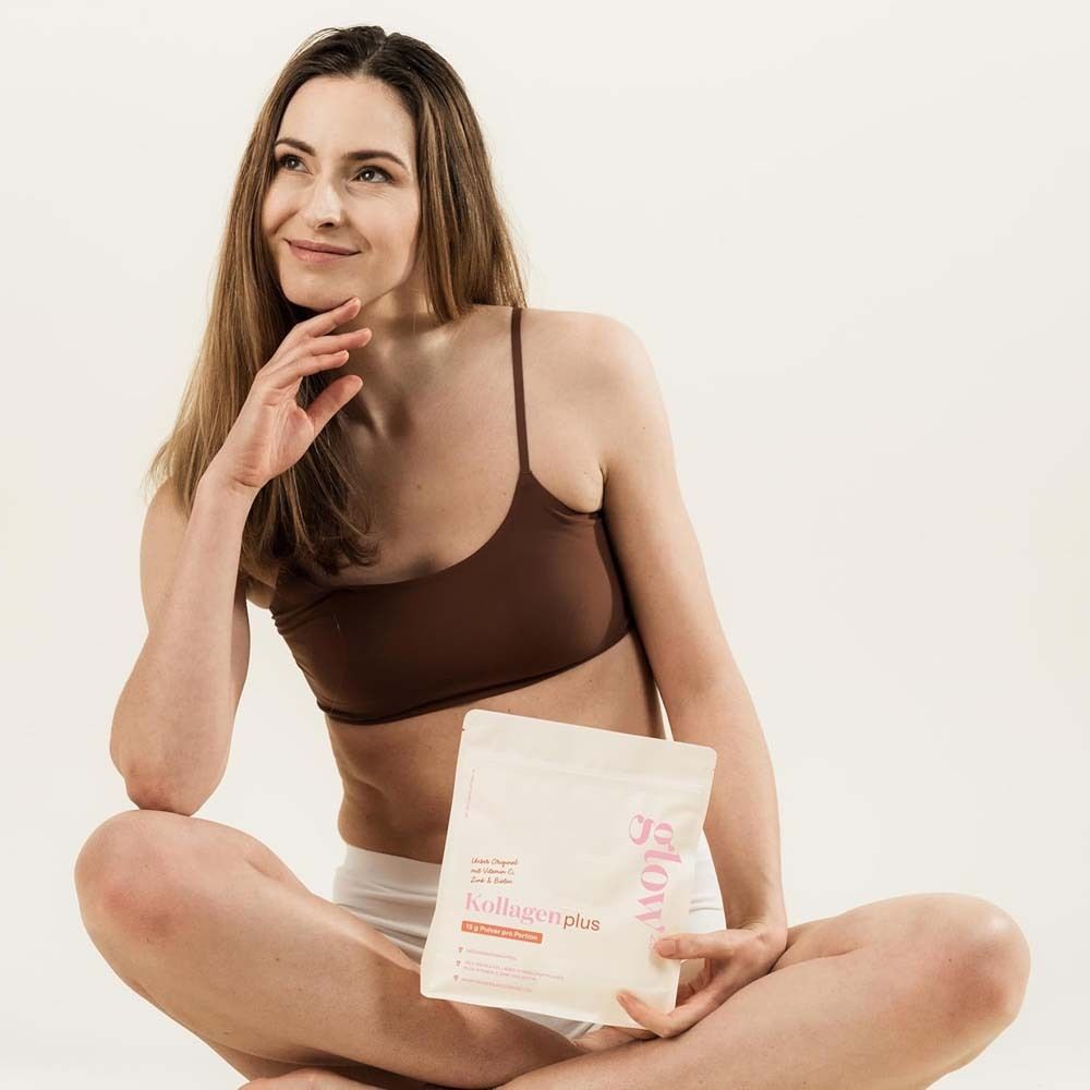 Frau sitzt mit Glow25® Kollagen plus-Beutel. Braunes Top, weiße Hose. Produktverpackung sichtbar.