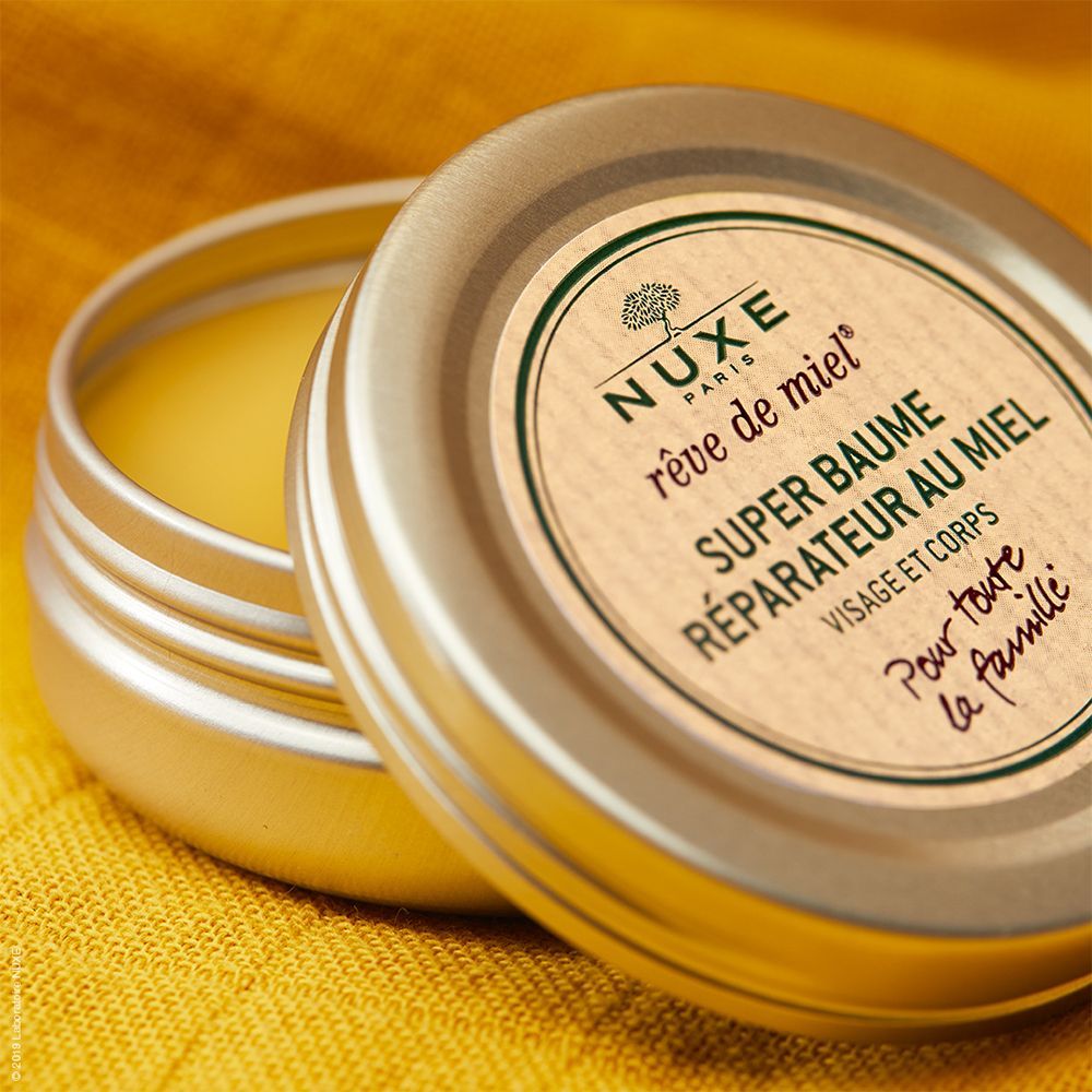 Pot rond ouvert. Étiquette avec nom et logo du produit. Baume jaune visible.